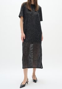 Svart paljettklänning med korta ärmar, knälång design, glansig textur och sidoklyftor. Bärs med svarta spetsiga tofflor.