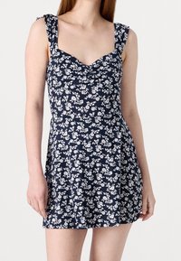 Navy blue floral dress with white patterns, featuring a fitted bodice, scoop neckline, and ruffled straps. Soft fabric and flared skirt.