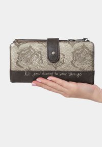 Cartera metálica dorada con un acabado texturizado, acentos de cuero marrón oscuro, cierre a presión y una frase en cursiva en la parte delantera.
