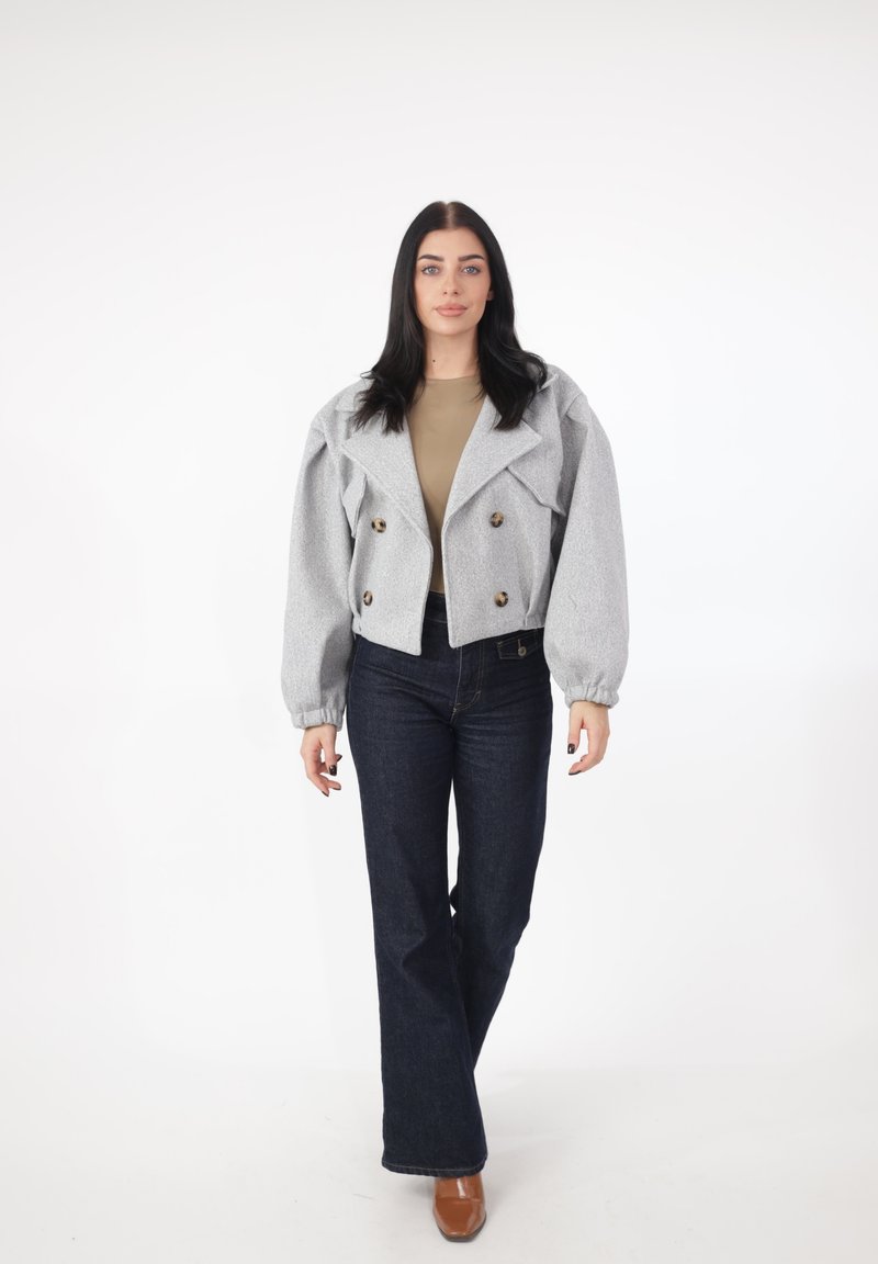 Grå, kort dobbeltradet jakke med store knapper, puffede ærmer, over en beige top og kombineret med mørkeblå vide jeans.