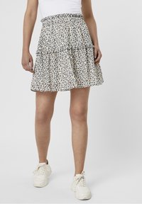 Vit flerad kjol med svart och orange blommönster, elastisk midja och ett lätt, flödande tyg. Bärs med vita sneakers.