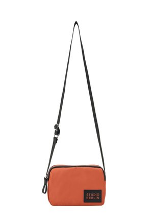 Kleine rechteckige orange Umhängetasche mit schwarzem verstellbarem Riemen und schwarzem Aufnäher mit der Aufschrift Studio Berlin vorne.