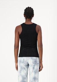 Top negro sin mangas con un diseño ajustado, escote redondo y tirantes, combinado con unos jeans de color azul claro con patrón de serpiente.