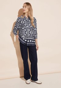 Camicia blu e bianca a fantasia con colletto, maniche lunghe e orlo curvo. Abbinata a pantaloni a gamba larga blu scuro e sneakers bianche.