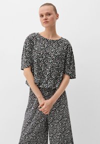 Schwarze Bluse mit floralem Muster, kurzen, weiten Ärmeln und lockerer Passform. Hat kleine weiße, rosa und grüne Blumen auf einem dunklen Hintergrund.
