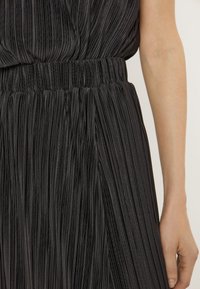 Vestito nero plissettato con una vita arricciata. Il tessuto ha una texture liscia con pieghe verticali, creando una silhouette fluente.