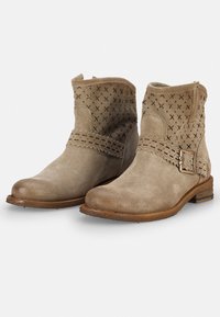 Botas de ante color topo hasta el tobillo con parte trasera texturizada, costuras decorativas, hebilla de metal y tacón bajo de madera; con patrón en X perforado en la parte superior.