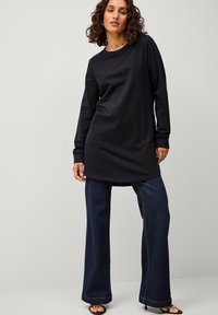 Zwarte lange mouwen tuniek top, ronde halslijn, gecombineerd met uitlopende donkerblauwe denim jeans. Losse pasvorm met een gladde textuur en een eenvoudig ontwerp.