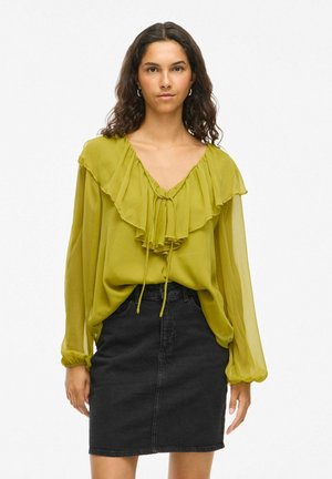 Langärmlige, olivgrüne Bluse mit Rüschenfront und Kordelzug, kombiniert mit einem schwarzen Denimsrock. Glattem, leichtem Stoff.