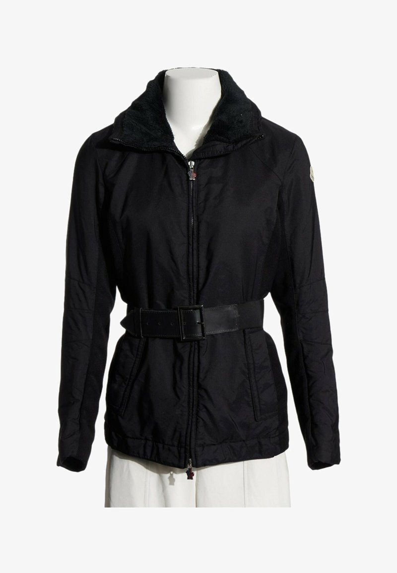 Veste noire ceinturée avec fermeture éclair sur le devant, deux poches avant et un col doux texturé sur un torse de mannequin blanc.