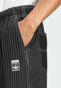 Black striped pants with an elastic waistband, featuring white pinstripes, a side pocket, and an Adidas logo tag.