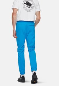 Pantalons de sport bleu vif en tissu léger, dotés de poignets élastiques et d'une texture lisse, associés à un t-shirt blanc imprimé.