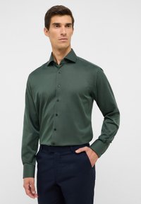Groene langemouwen shirt met een subtiel textuurpatroon, knopen aan de voorkant en een klassieke kraag, gecombineerd met marineblauwe broek.