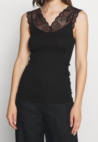 Svart ribbad linne med genomskinlig spetskrage och vågiga kanter, prydd med blommönster i rött och svart. Utan ärmar.