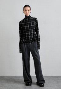 Maglione a collo alto a quadri in bianco e nero con dettagli arricciati ai lati, abbinato a pantaloni larghi grigi e scarpe con zeppa nere.