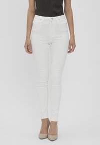 Jean skinny blanc taille haute, en denim. Le tissu a une texture lisse, associé à des chaussures à talons hauts beige.