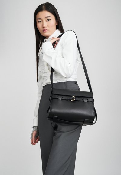 Schwarze Lederhandtasche mit strukturiertem Design, goldenen Hardware-Akzenten und verstellbarem Riemen; glatte Textur mit einer Schnallen-Detail.