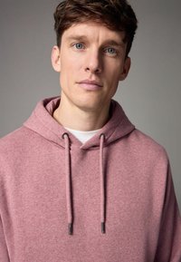Sudadera con capucha de suave tela rosa, con un bolsillo tipo canguro, cordones con puntas plateadas y un corte relajado.