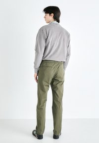 Camisa gris de manga larga con un corte relajado, combinada con pantalones olive verdes de cintura elástica, que exhiben una textura suave y un diseño simple.