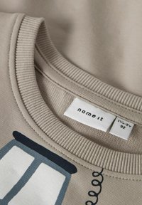 Felpa beige con scollo girocollo a costine. Presenta una grafica di porte in blu scuro e grigio chiaro. L'etichetta riporta "name it" e la taglia.