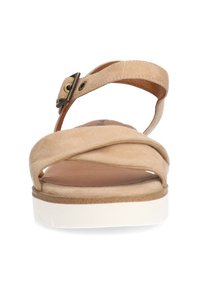Beige suède sandaal met kruislings straps, verstelbare gesp en een witte plateauzool. Gladde textuur en casual ontwerp.