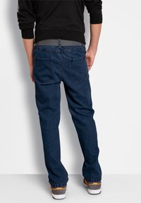 Jeans in denim blu scuro con taglio dritto, due tasche posteriori e una cintura grigia, abbinati a sneakers basse.