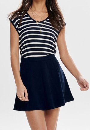 Femme portant un haut à manches courtes rayé bleu marine et blanc, rentré dans une jupe évasée unie bleu marine, accessoirisée de colliers dorés superposés.