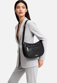 Borsa nera trapuntata con dettagli in oro, caratterizzata da una silhouette curva e una tracolla staccabile. Logo ben visibile sul davanti.