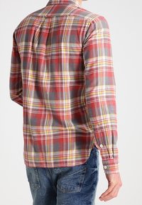Camicia a maniche lunghe a scacchi rossi e grigi con dettagli gialli, polsini con bottoni e colletto classico, caratterizzata da una trama di tessuto morbido.
