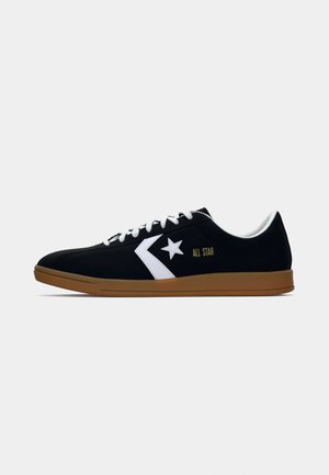Sorte lærredssneakers med hvide detaljer, der har et stjernelogo og teksten "ALL STAR". Gummiydersålen er lysebrun. Klassisk lavtopdesign.