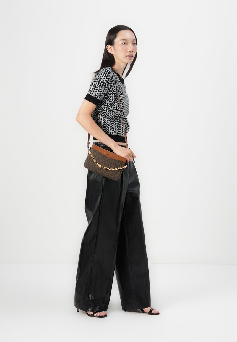 Gewebtes Oberteil mit schwarz-weißen Mustern, hochgeschnittene schwarze Kunstlederhosen und eine braune Umhängetasche mit goldener Kettendetails.