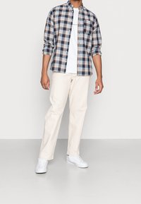 Camicia a quadri in blu, bianco e arancione con chiusure a bottone, abbinata a pantaloni color crema e sneakers bianche. Vestibilità semplice e rilassata.