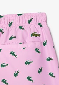Pantaloni corti rosa chiaro con elastico in vita, caratterizzati da un motivo ripetuto di coccodrilli verdi e un piccolo logo coccodrillo ricamato.