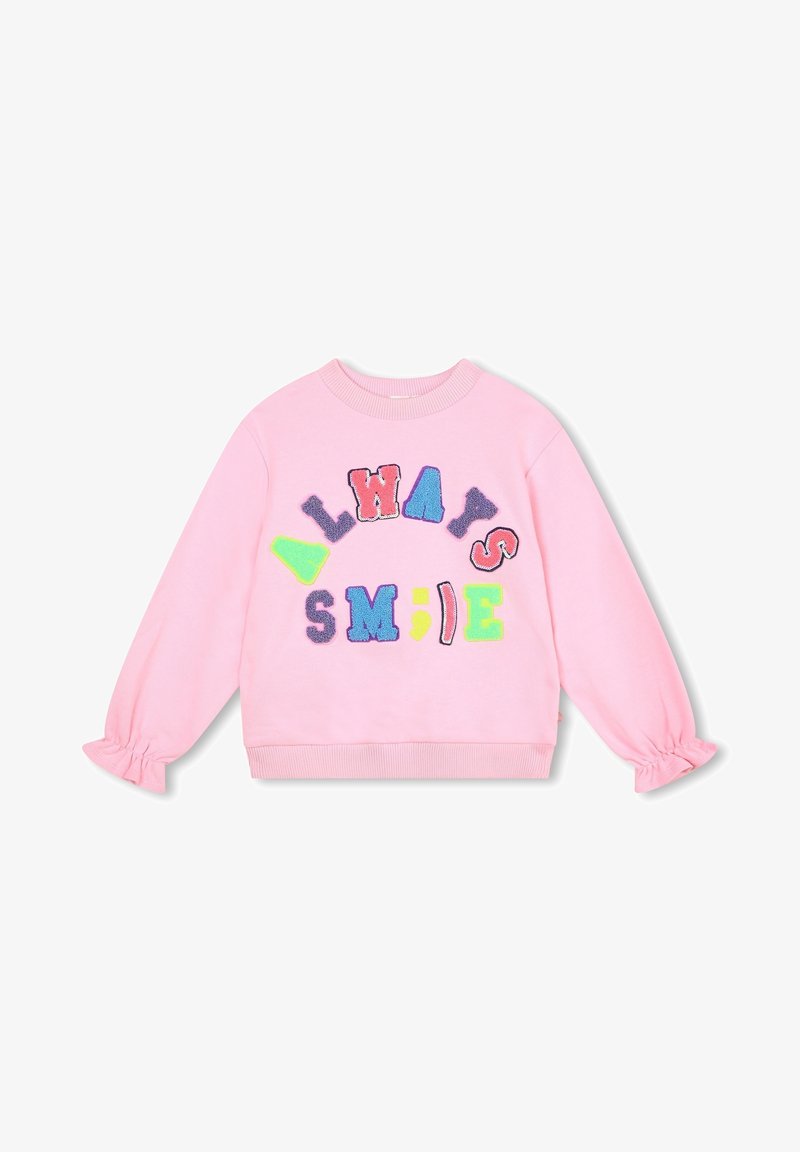 Pull rose à manches longues avec des poignets à volants et des lettres texturées colorées formant les mots "TOUJOURS SOURIRE" en arc de cercle et en ligne sur le devant.