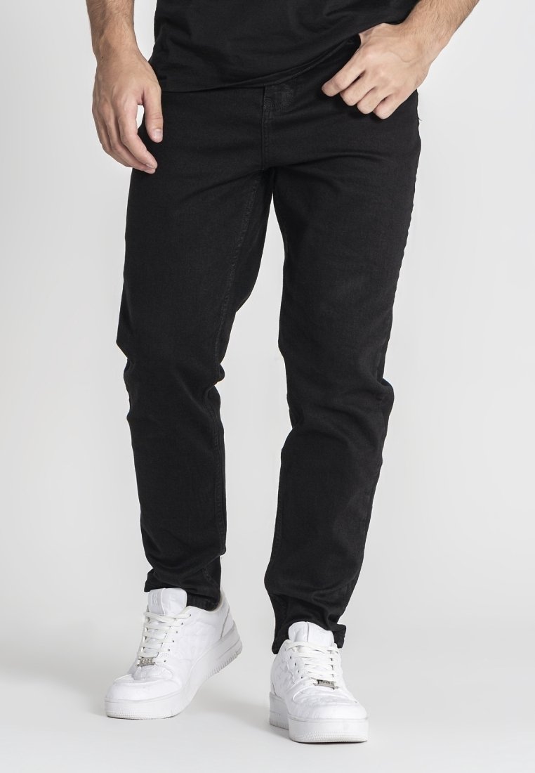 Jeans de denim negro con corte ajustado y una textura sutil, combinados con zapatillas blancas con un acabado liso y suela prominente.