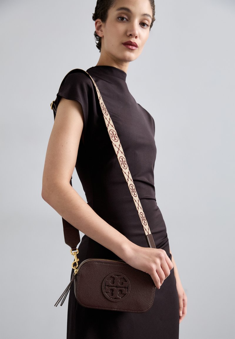 Brown leather crossbody bag with embossed logo. Features a patterned strap in beige and maroon, zip closure, and a decorative tassel.