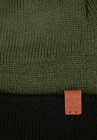 Zimowa czapka z dzianiny w oliwkowym zielonym i czarnym kolorze. Posiada prążkowaną teksturę oraz skórzaną metkę z napisem "Bickley + Mitchell."