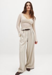 Bežinė tekstūruota ilgomis rankovėmis palaidinė derinama su aukštu liemeniu šviesiai bežinėmis klostuotomis kelnėmis ir tamsiai rudos spalvos plokščiais batais. Diržas su metaliniais elementais.