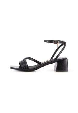 Sandalia de cuero negro con tacón ancho, puntera cuadrada, tiras delanteras cruzadas y correa en el tobillo con pequeña hebilla dorada y charm.