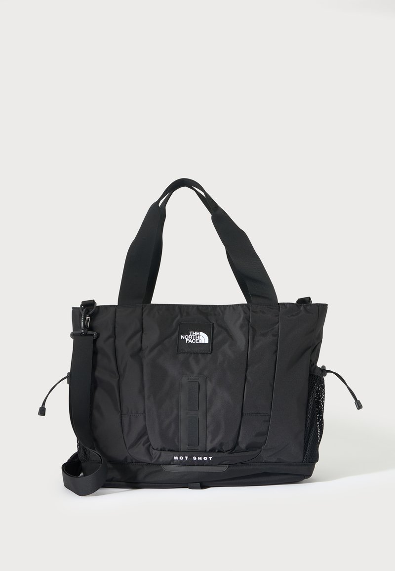 Μαύρη τσάντα tote The North Face με δύο χερούλια, ρυθμιζόμενο ιμάντα ώμου, δίχτυ πλαϊνή τσέπη και κείμενο "HOT SHOT" στο κάτω μπροστινό μέρος.
