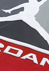 Il tessuto nero, grigio e rosso presenta un logo silhouette bianco texturizzato e la scritta in grassetto "JORDAN", evidenziando un design a strati.