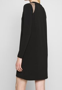 Musta pitkähihaiseksi mekko, jossa on rento istuvuus, tekstiilinen verkko takapaneeli ja pyöreä kaula-aukko. Pehmeä kangas ja keskimittainen pituus reiden keskivaiheille.