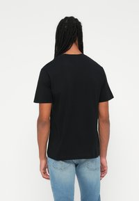 Juodas medvilninis T-shirt su trumpomis rankovėmis ir klasikiniu apvaliu kaklu. Lygus paviršius, be matomų raštų ar akcentų. Dėvima su šviesiai mėlynomis džinsinėmis kelnėmis.