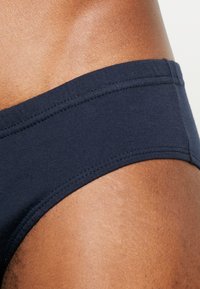 Navyblaue Baumwollslips mit einem breiten elastischen Bund, ausgestattet mit glatter Stoffoberfläche und detailliertem Stich entlang der Kanten.