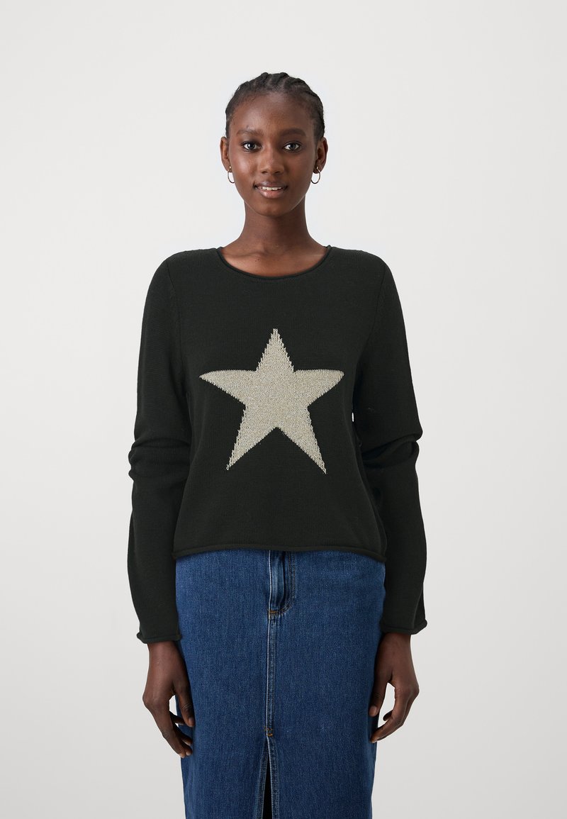 Pull noir à manches longues avec une grande étoile en tricot argentée sur le devant. Assorti à une jupe en denim, mettant en valeur une fente.
