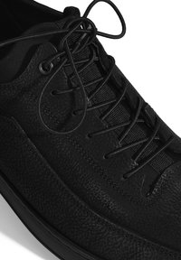 Baskets noires avec tige en cuir texturé, lacets ronds et languette rembourrée. Présente un design épuré et une semelle en caoutchouc fine.