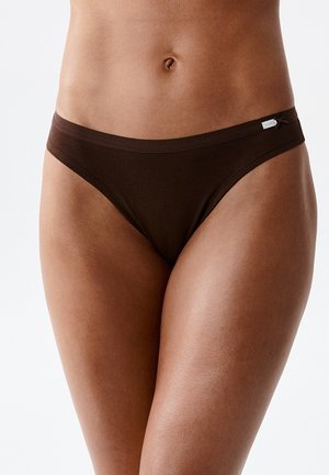 Środkowa część kobiecego ciała ubrana w ciemnobrązową bieliznę bikini na jednolitym białym tle.