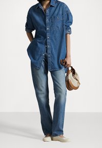 Dunkelblaues Denimhemd mit langen Ärmeln, Knopfverschluss und Brusttasche; kombiniert mit hellblauen Jeans und einer kleinen braunen und beigen Handtasche.