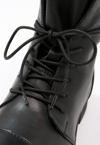 Bottes en cuir noir à bout rond. Elles présentent des lacets robustes, une texture lisse et des détails cousus sur le capuchon et les côtés.