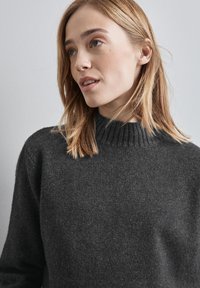 Kolgrå tröja med hög ribbad krage och mjuk textur, med långa ärmar och avslappnad passform. Minimalistisk design utan mönster.